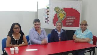 Mujeres en una mesa  rectangular roja dando una charla.