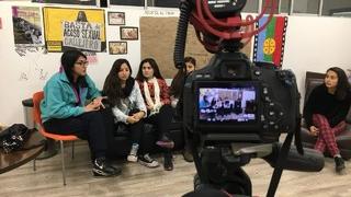 Cámara grabando a un grupo de universitarias conversando en una reunión.