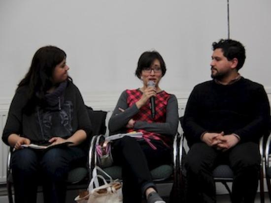 tres personas sentadas, la mujer del medio habla por micrófono.