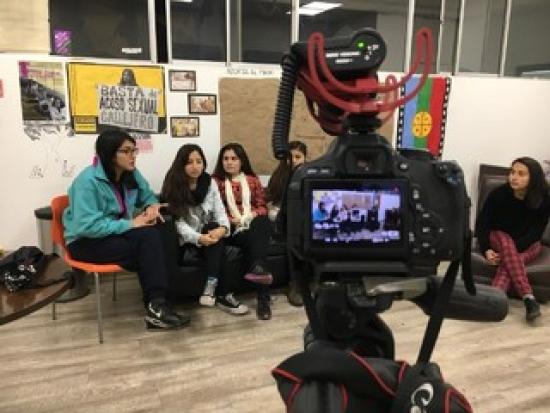 Cámara grabando a un grupo de universitarias conversando en una reunión.