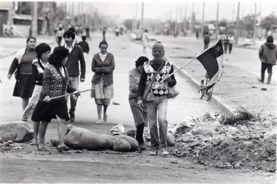 Pobladoras caminando junto a una barricada, sosteniendo una de ellas una bandera de Chile. S/f. Fondo Archivo Fotográfico Fortín Mapocho. CL ARNAD AD-10-FFMAP-S56-FOT/FM B(04051). Archivo Nacional de la Administración. Fotografía.